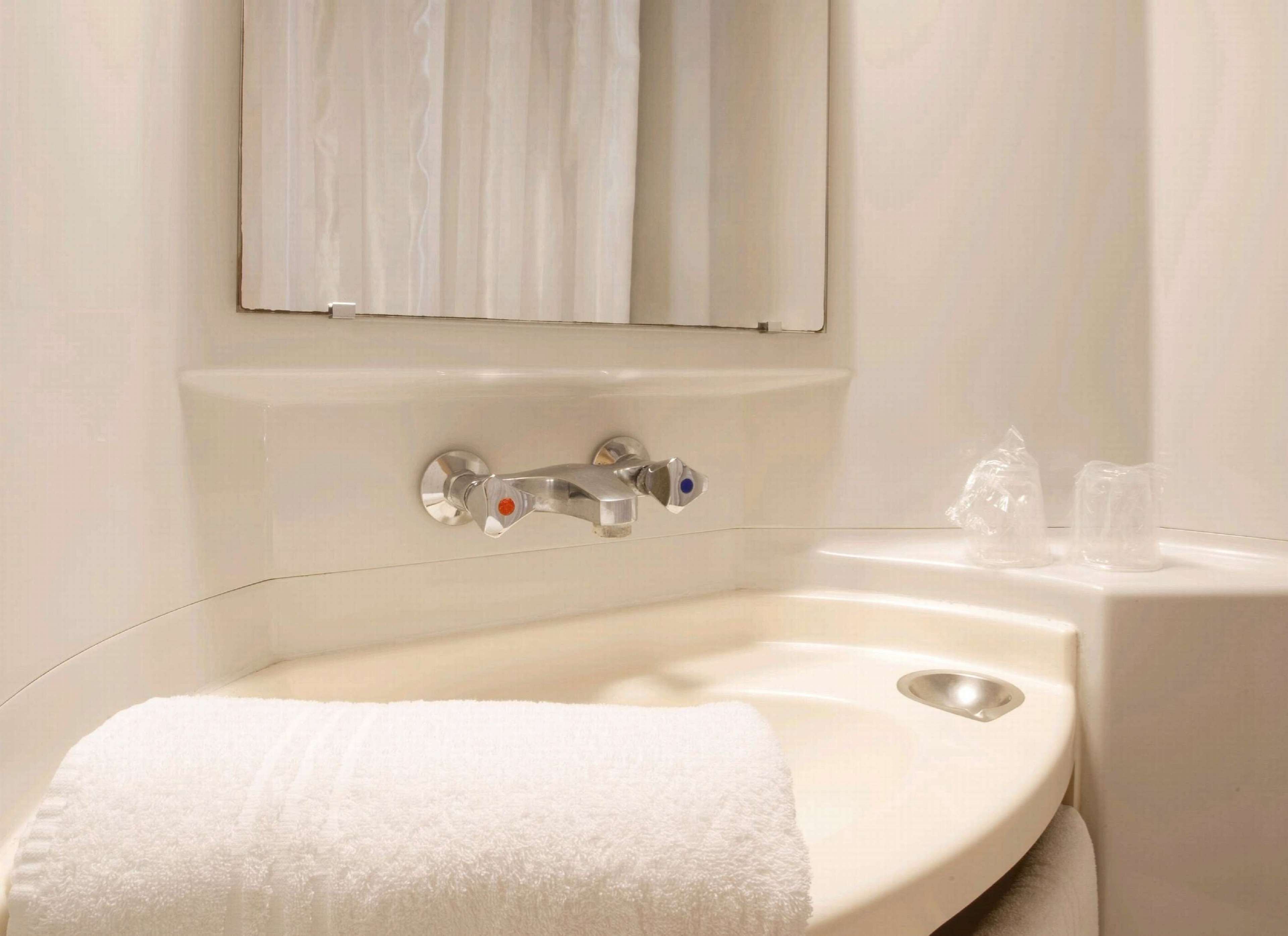 Un bagno con un lavandino bianco, uno specchio e un asciugamano.