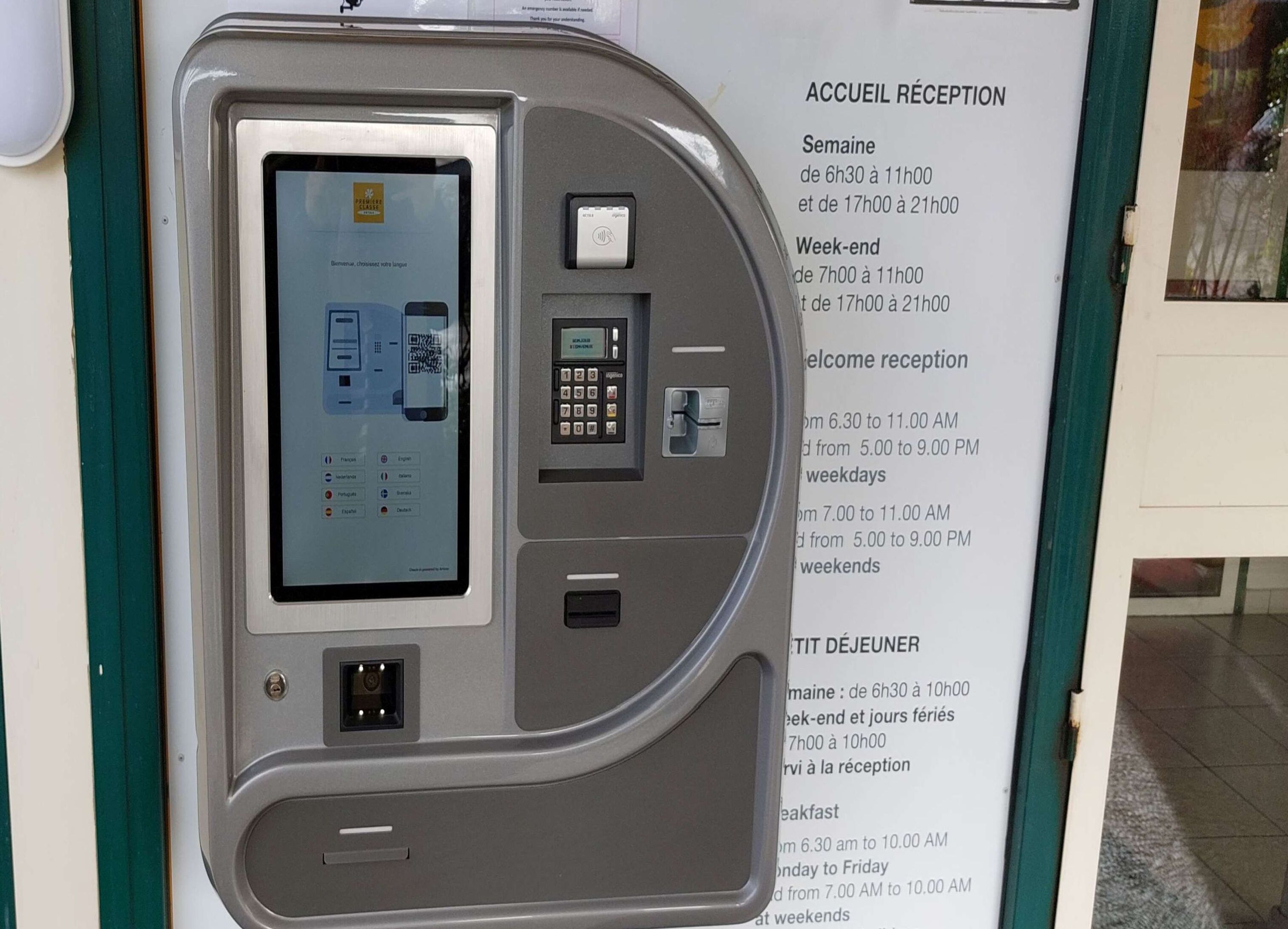 Un quiosco de autoservicio con pantalla y teclado, junto a un cartel que indica el horario de recepción.