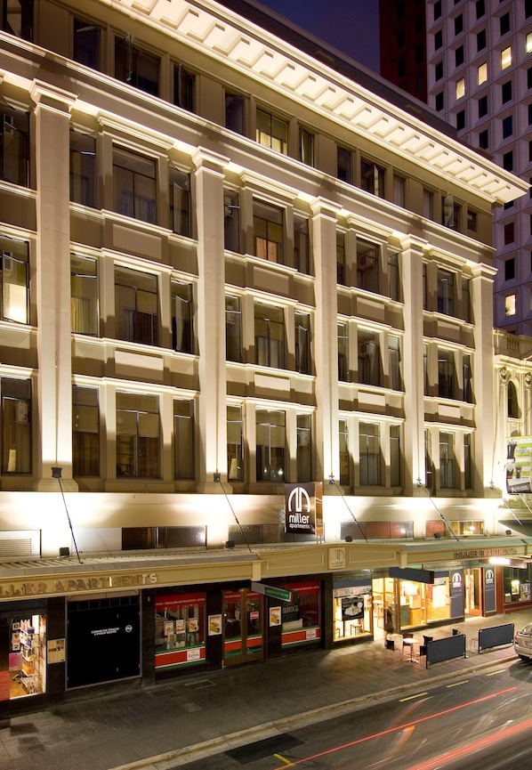 A multi-story hotel with a classic architectural design, featuring large windows and a well-lit facade.