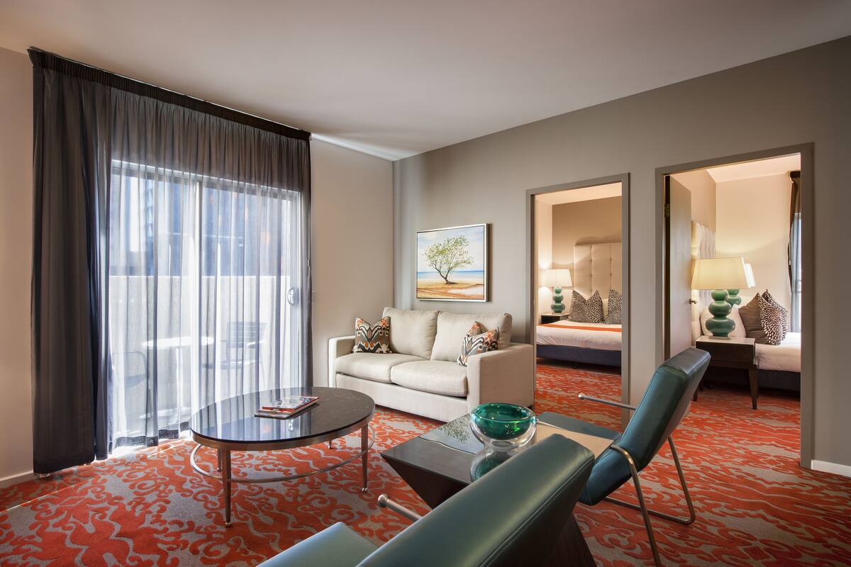 Habitación de hotel con sofá, una mesa de centro de vidrio, una silla, cama y un cuadro en la pared.
