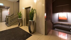 A modern hotel lobby with a staircase, large potted plants, a reception desk, and a wall-mounted TV. - Miller Apartments Adelaide (Adelaide)