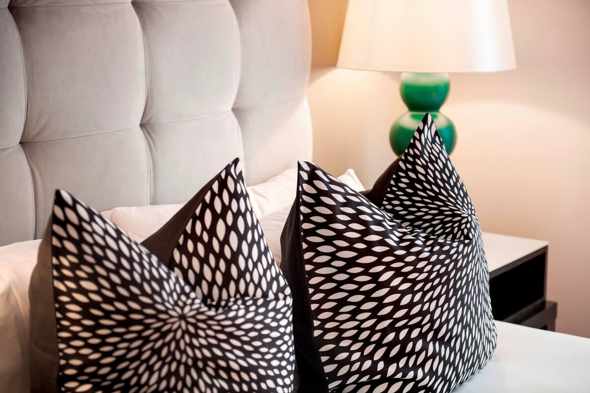 Una cama con cabecera capitonada y dos almohadas decorativas con estampado geométrico.