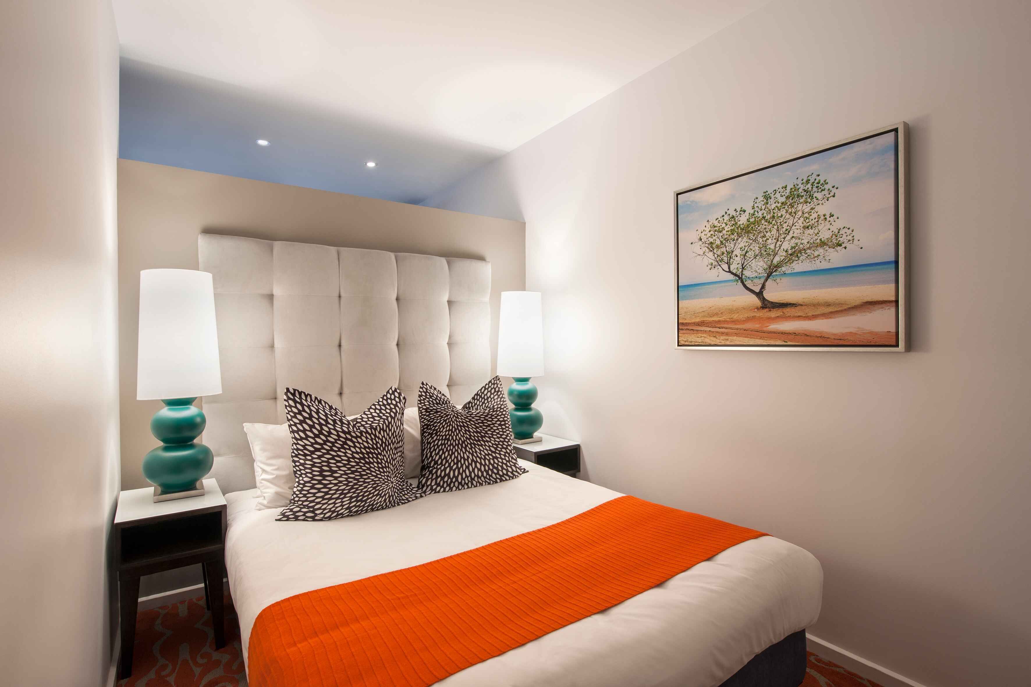 Un dormitorio con una cama grande, dos mesitas de noche, un cabecero y un cuadro de un árbol en la pared.