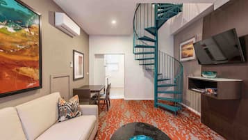 Un salon moderne avec un canapé, un escalier, un téléviseur à écran plat et un tableau accroché au mur.