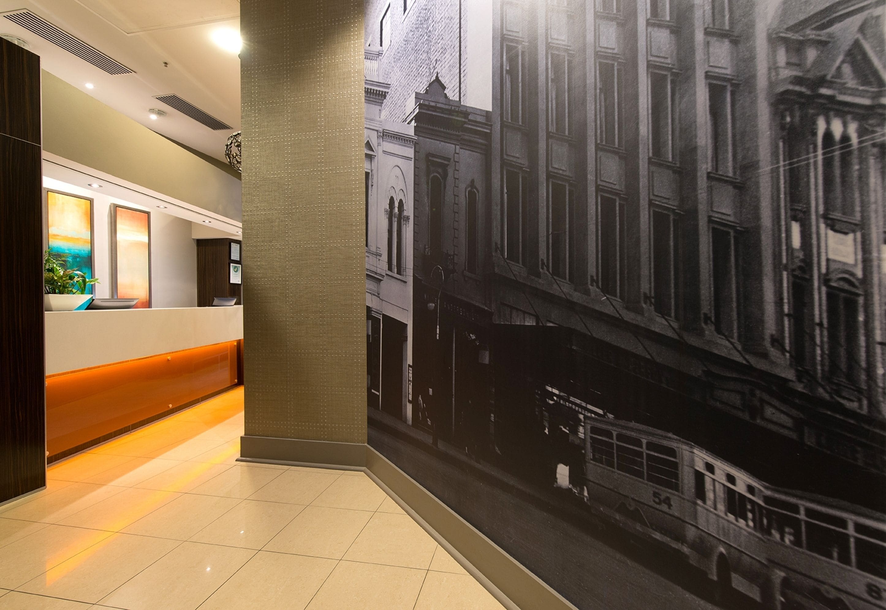 A hotel reception area with a modern design, a reception desk, and a large black and white photograph of a historic street scene on the wall.