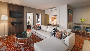 A modern living room with a sectional sofa, a glass coffee table, and a dining area with blue chairs. - Miller Apartments Adelaide (Adelaide)