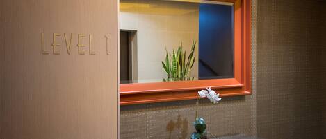 A bathroom with a wooden vanity, a mirror with an orange frame, and a potted plant with white flowers.