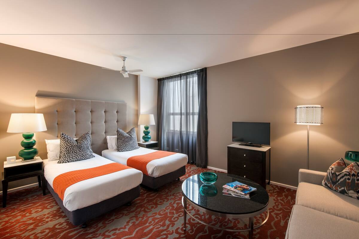 Habitación de hotel con dos camas, televisión, mesa de centro y sofá.