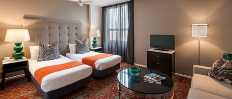 A hotel room with two beds, a TV, a coffee table, and a sofa.