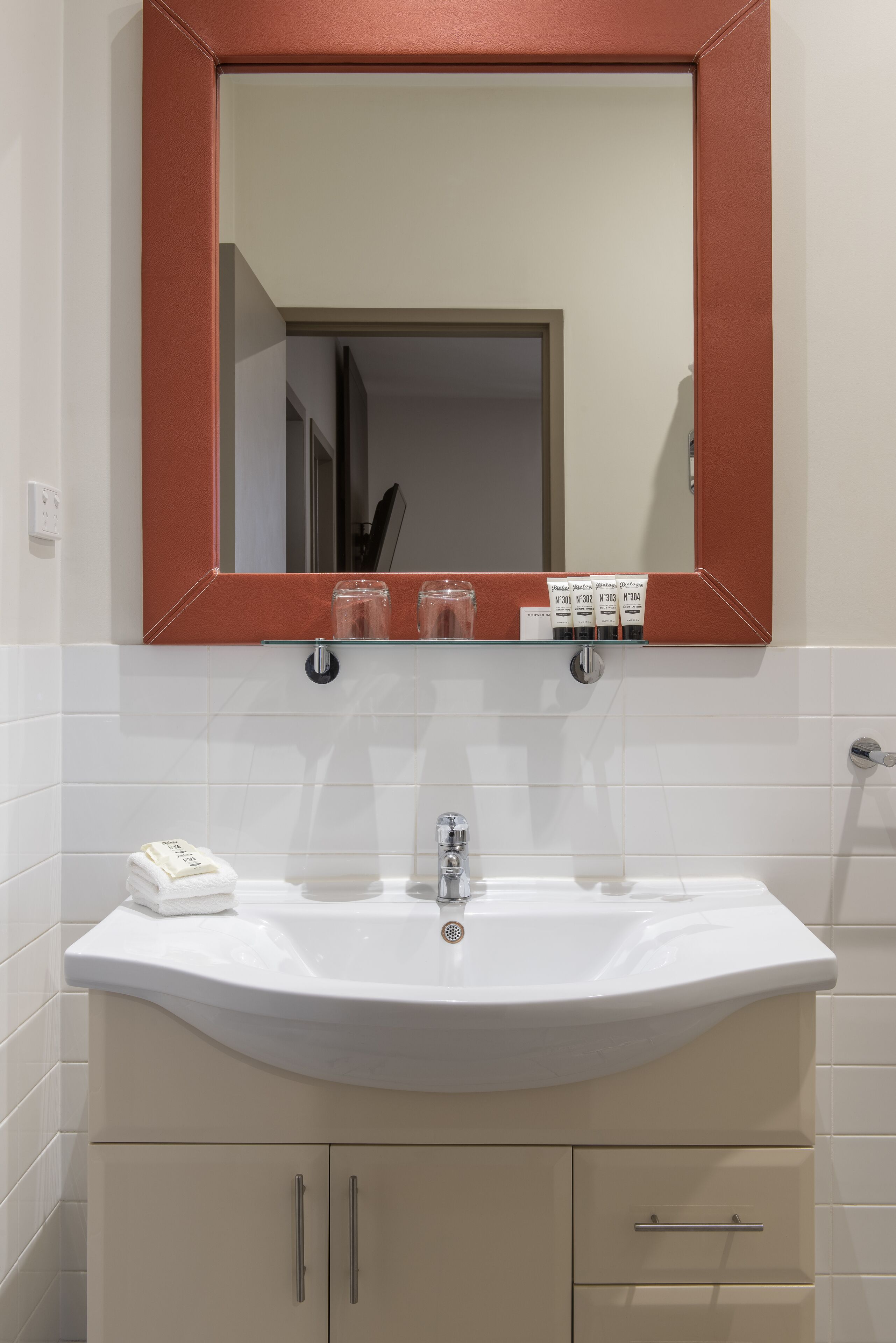 Un bagno con un lavandino bianco, uno specchio con cornice rossa e un portascopevoli.
