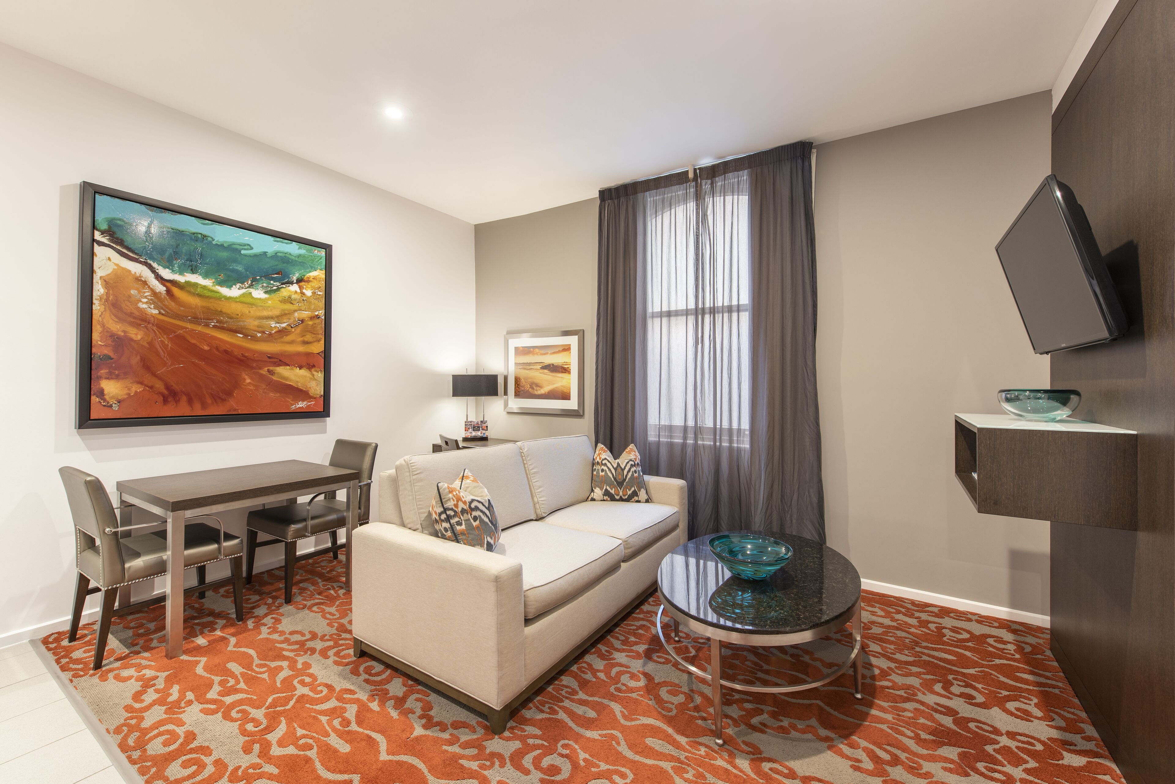 A modern living room with a sofa, dining table, chairs, a coffee table, and a large abstract painting.