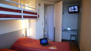 Una habitación de hotel con literas, una computadora portátil sobre una cama, un escritorio pequeño con una silla y un televisor montado en la pared.