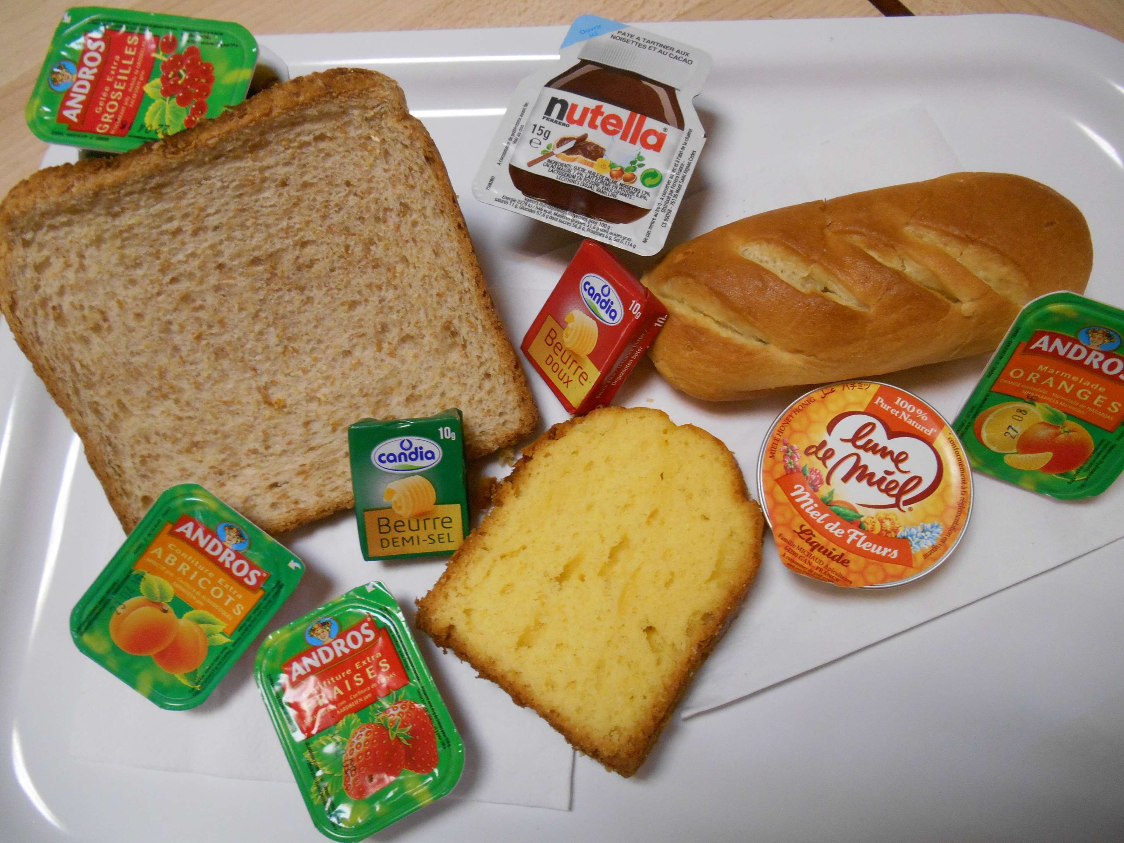 Diversos alimentos como pão, Nutella e geleias de fruta em um prato.