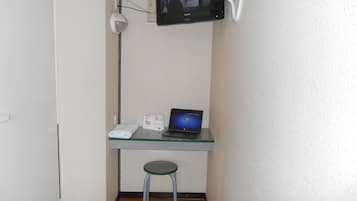 A small room with a glass desk, a laptop, a security camera, and a white towel on the floor.