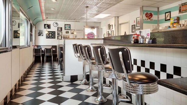 A diner interior with a checkered floor, bar stools, a counter, and a ceiling with a grid pattern. - Travelodge by Wyndham Dunsmuir (Dunsmuir)