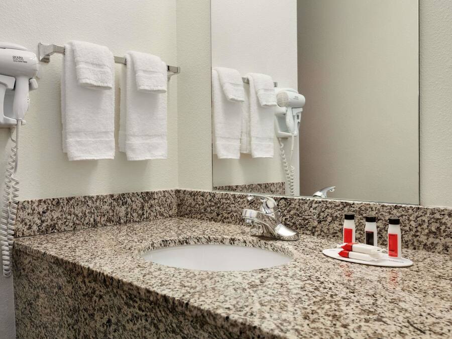 Un baño con encimera de granito, un lavabo, un espejo, dos secadores de pelo y tres botellas de artículos de aseo.