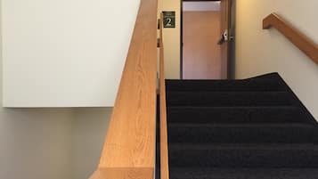 A wooden handrail next to a carpeted staircase leading to a door marked "Level 2, Star 8, Roof Access 2, 1 Through 2".