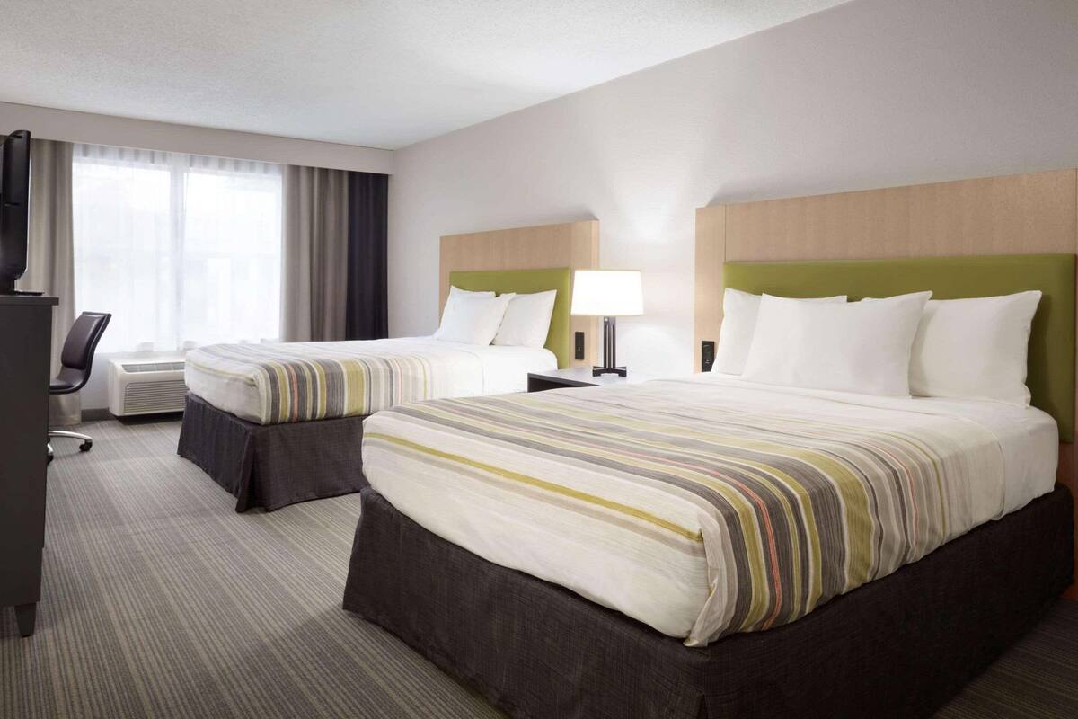 A hotel room with two beds, a desk, and a chair.