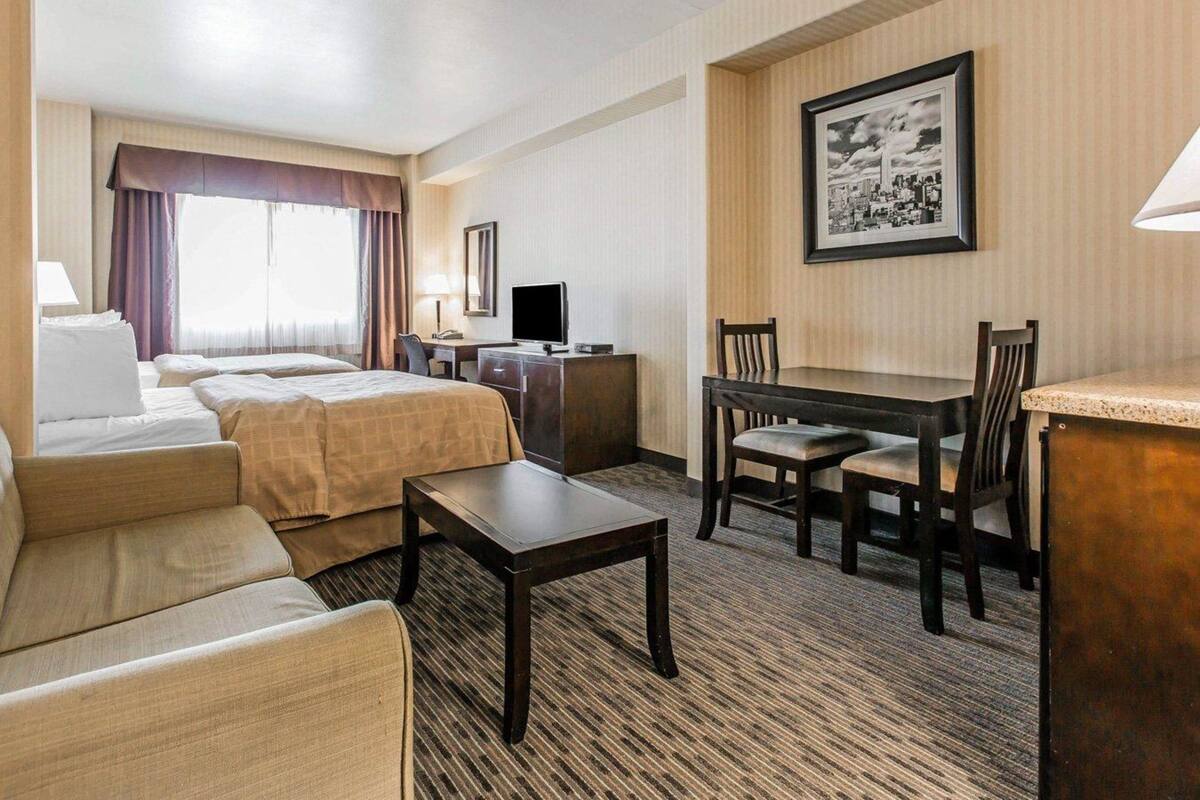 Une chambre d’hôtel avec un lit, un bureau, une chaise, une table et un tableau encadré au mur.