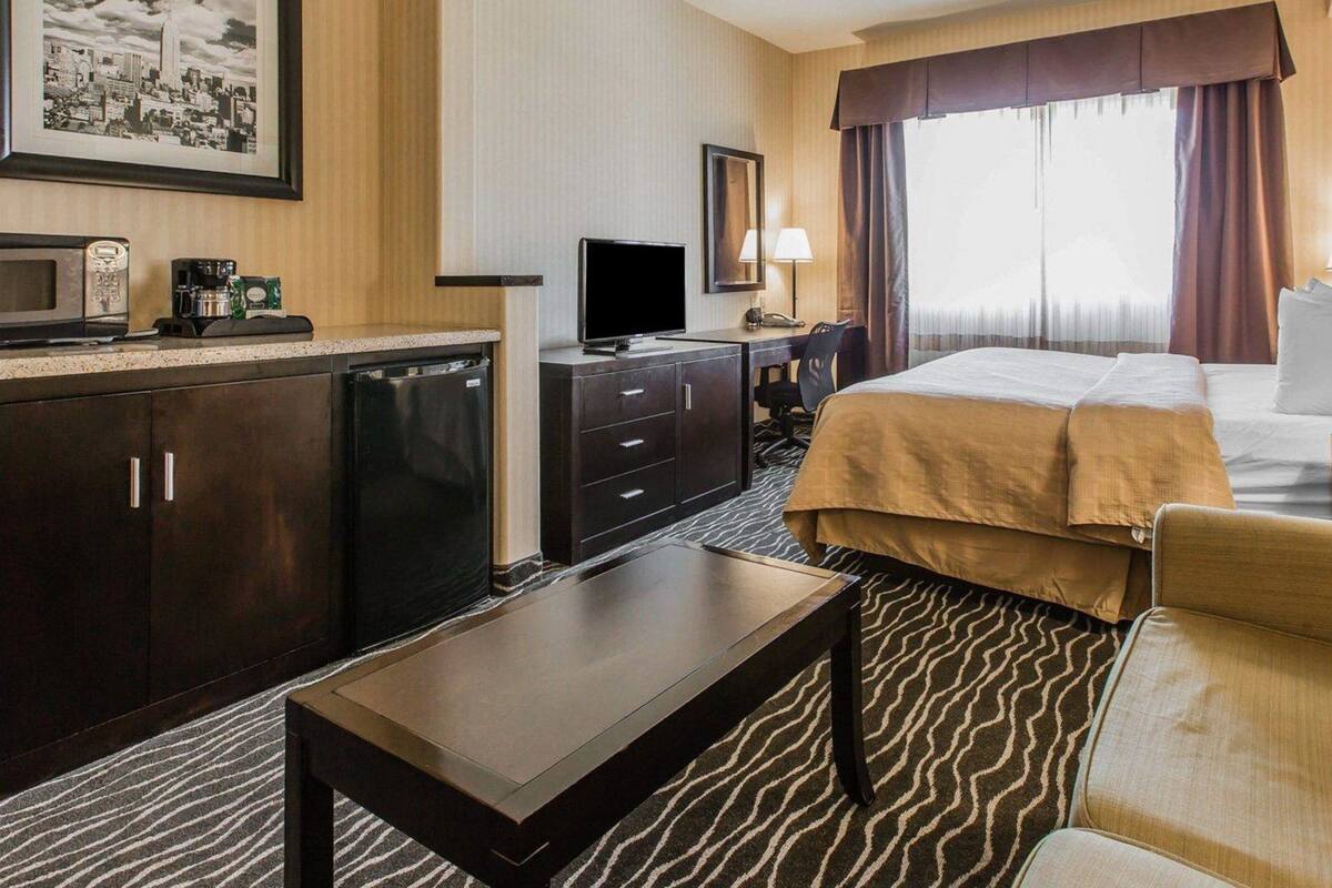 Une chambre d’hôtel équipée d’un lit, d’un bureau, d’une télévision, d’une machine à café et d’un tableau représentant une vue panoramique de la ville, accroché au mur.