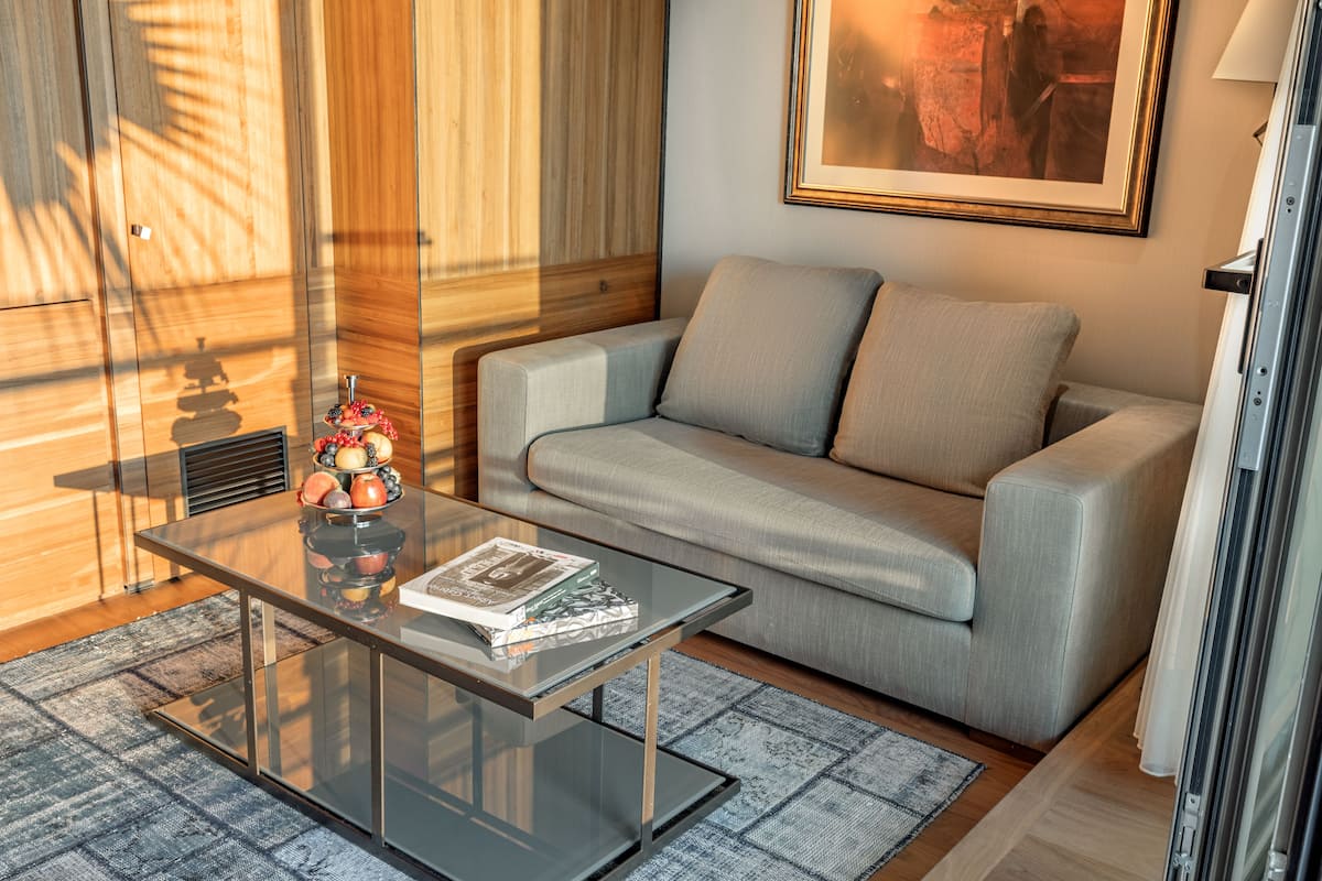 A modern living room with a glass coffee table, a grey sofa, and a framed picture on the wall.