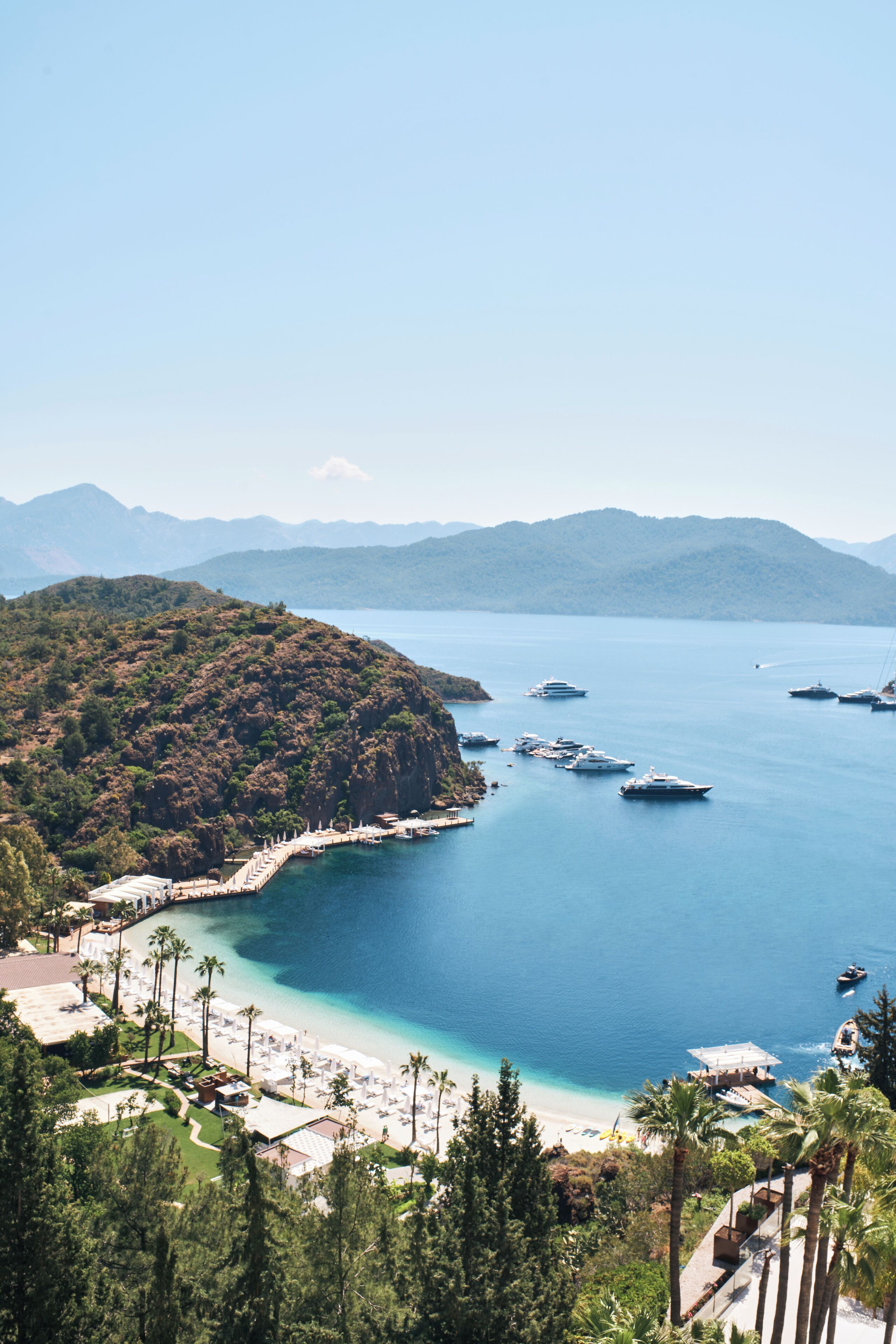 Un complejo turístico en la costa con playa, aguas azules cristalinas y barcos.
