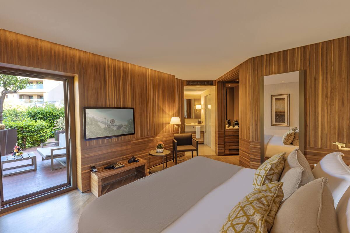 A modern hotel room with a large bed, a television, a desk with a lamp, and a view of the outdoors.