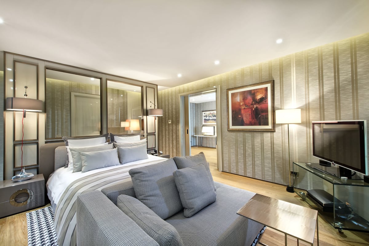 A modern hotel room with a large bed, a sofa, a TV, and a painting on the wall.