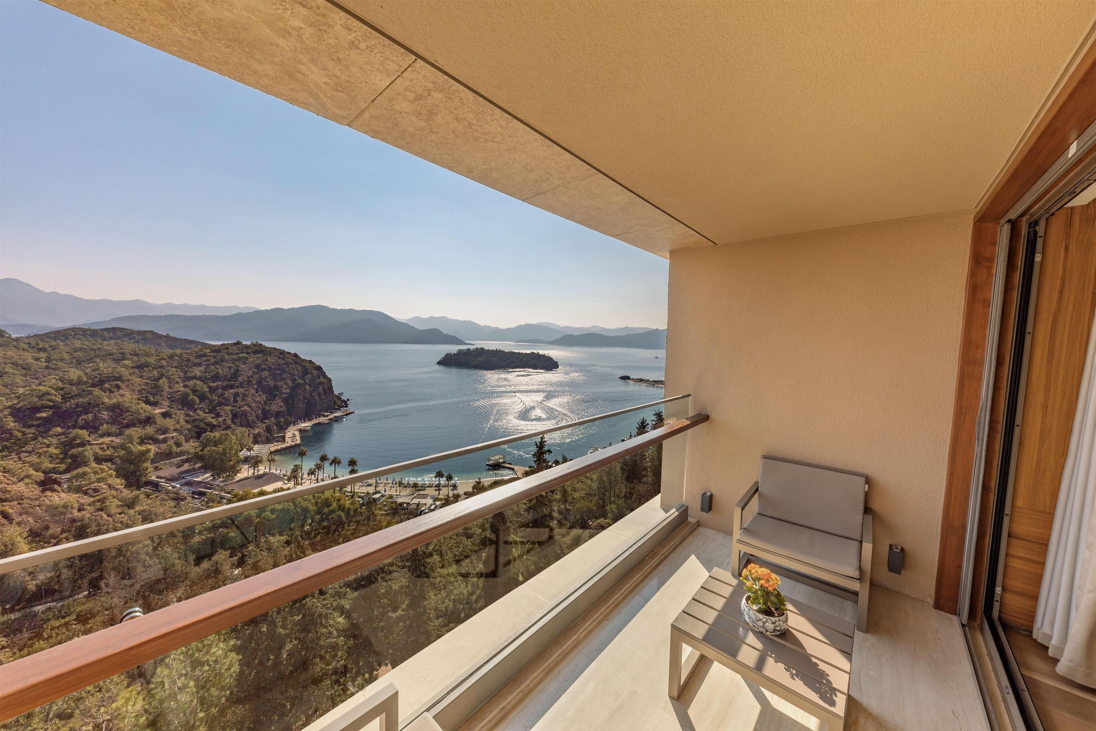 Un balcon offrant une vue sur un paysage côtier, comprenant une étendue d’eau et des montagnes lointaines.