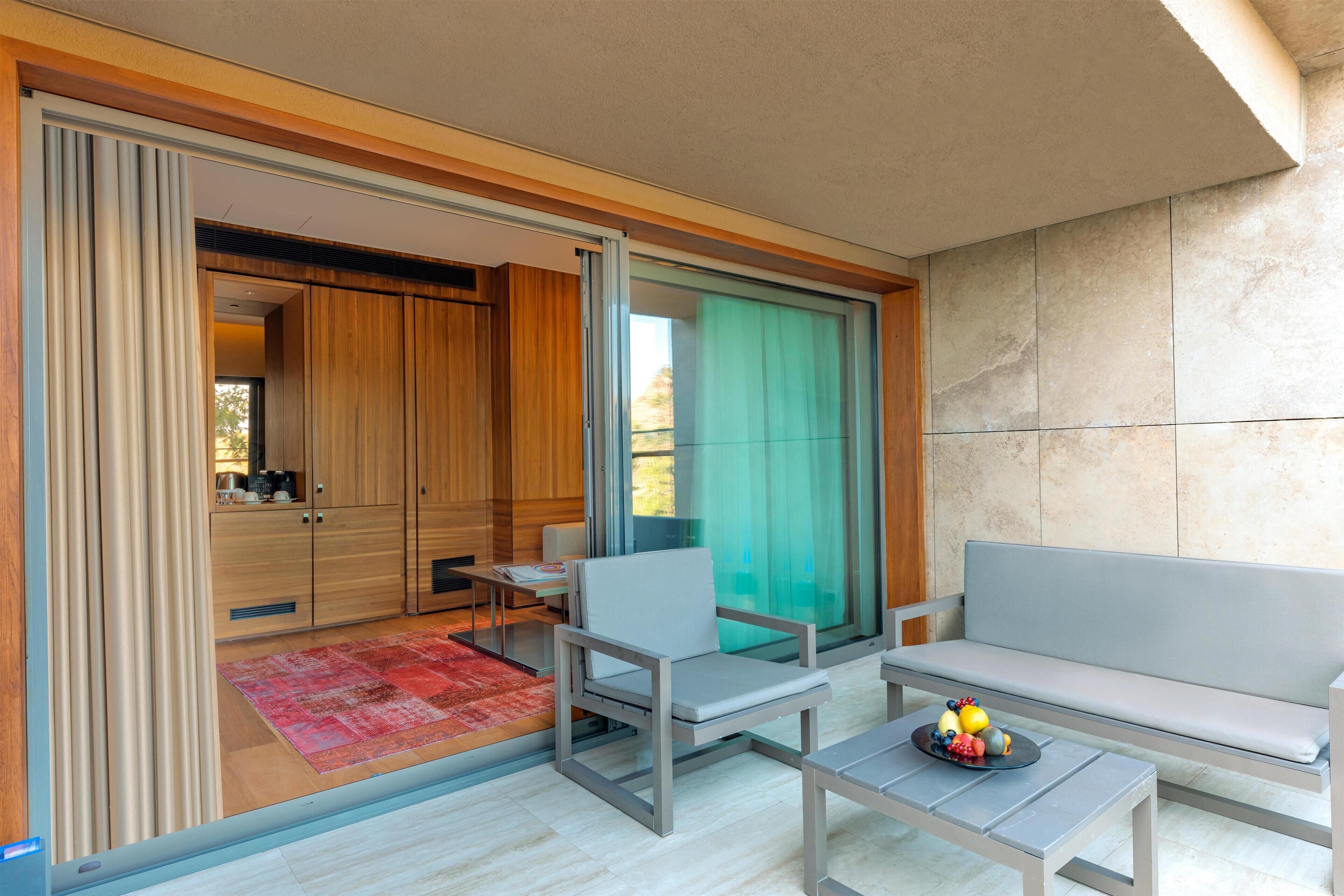 Uma sala de estar moderna com um sofá, uma mesa de centro e uma poltrona. Há uma porta de vidro deslizante que dá para uma área de cozinha.