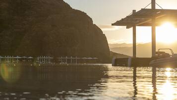 A waterfront scene with a pier, boats, and a mountainous backdrop during sunset.