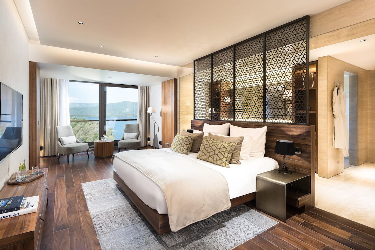 A modern hotel room with a large bed, a TV, a desk, and a balcony with a view.