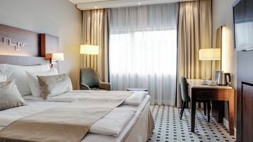 A hotel room with a large bed, two bedside tables, a desk with a chair, a television, and a window with curtains.