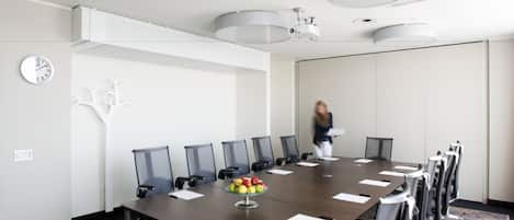 A conference room with a long table, chairs, a clock, and a fruit bowl.
