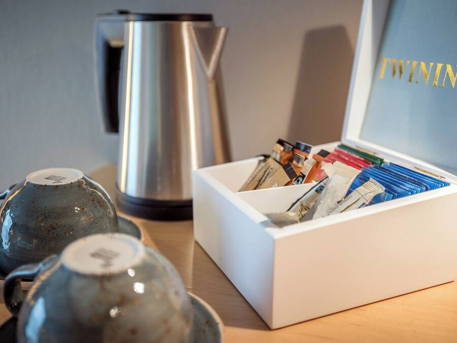 A white box with a label reading "TWININGS" containing various items, a metal kettle, and two ceramic teapots on a wooden surface.