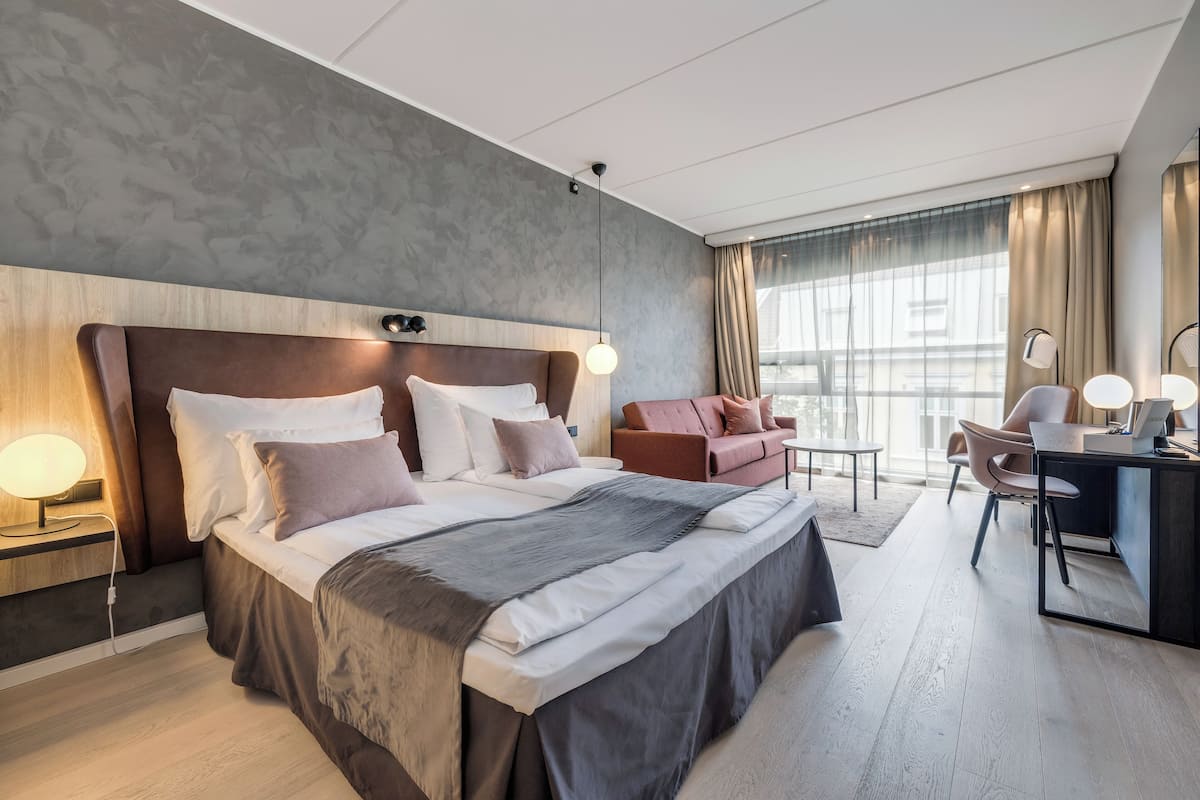 A modern hotel room with a large bed, a desk, and a sofa.
