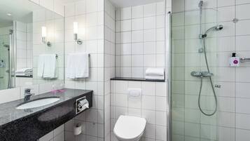 Un baño moderno con encimera de granito, lavamanos blanco, inodoro y cabina de ducha con paredes de vidrio.
