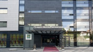 Una entrada de hotel moderna con alfombra roja, fachada de vidrio y un letrero que dice 'Quality Hotel Fredrikstad'.
