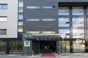 Una entrada de hotel moderna con alfombra roja, fachada de vidrio y un letrero que dice 'Quality Hotel Fredrikstad'.