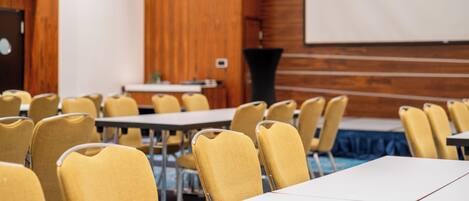 Una sala de conferencias con sillas, mesas y una pantalla para proyector amarillas.