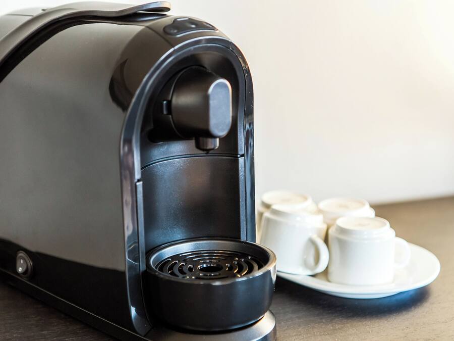 Una cafetera con una perilla de control y una bandeja de goteo, acompañada de cuatro tazas de café blancas sobre un plato.