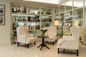 Una habitación con tres sillones blancos, una mesa redonda pequeña y un aparador de cristal lleno de botellas y objetos decorativos.