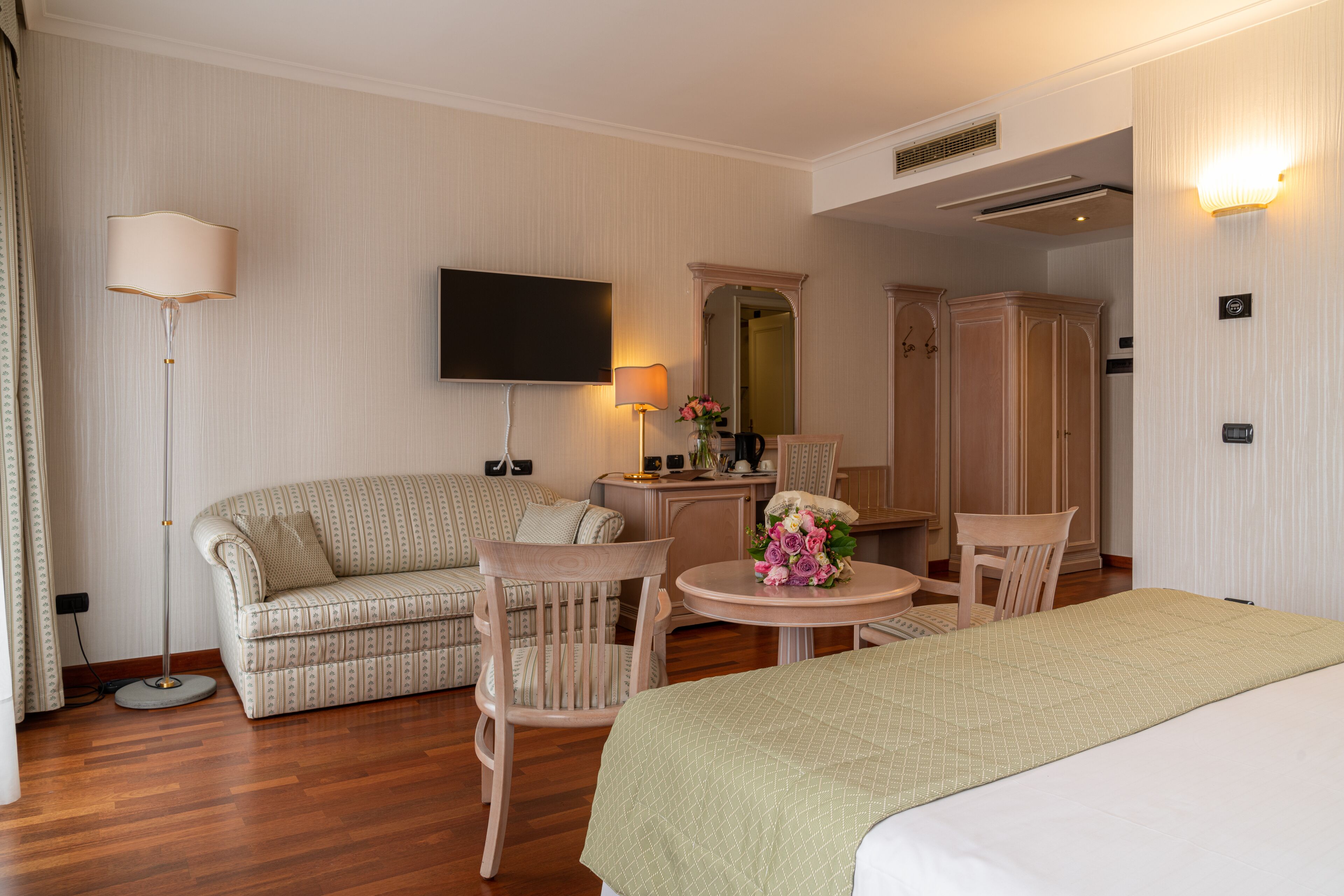 Habitación de hotel con cama, sofá, dos sillones, una mesita, televisión, espejo y lámpara.