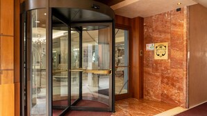 A revolving door with glass panels and a brass handle, leading to a lobby with a marble floor and a sign on the wall. - Hotel Roxy Plaza (Soave)