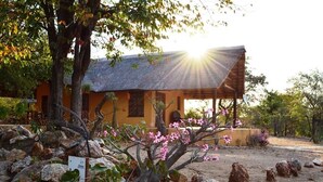 A rustic building with a thatched roof, surrounded by rocks and flowering plants.