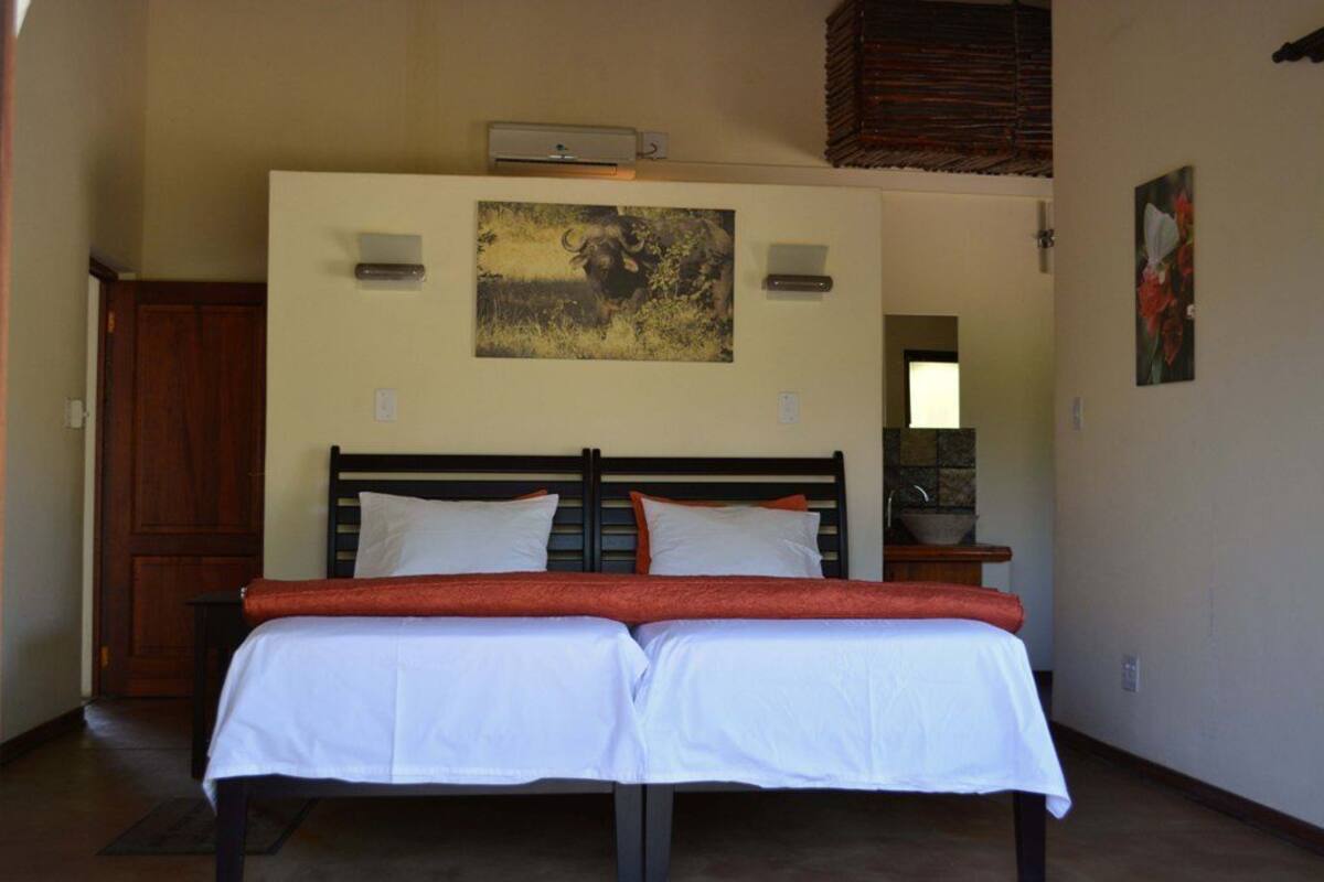 A double bed with white and orange bedding, a wooden headboard, and a wall-mounted picture.
