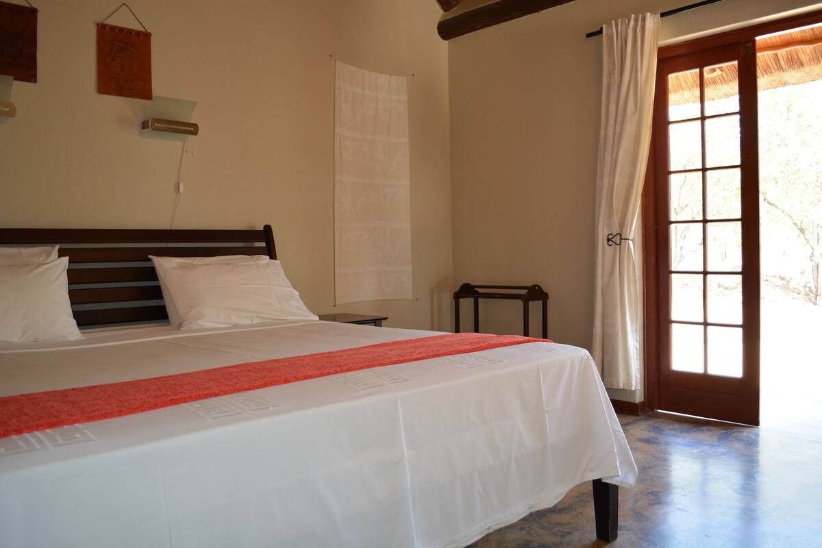 A bedroom with a bed, a nightstand, a window with curtains, and a door.