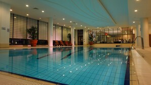 An indoor swimming pool with tiled walls, benches, and potted plants.