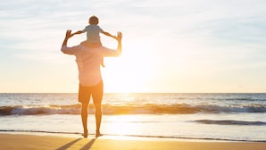 Una persona lleva a un niño sobre sus hombros en la playa durante el atardecer.