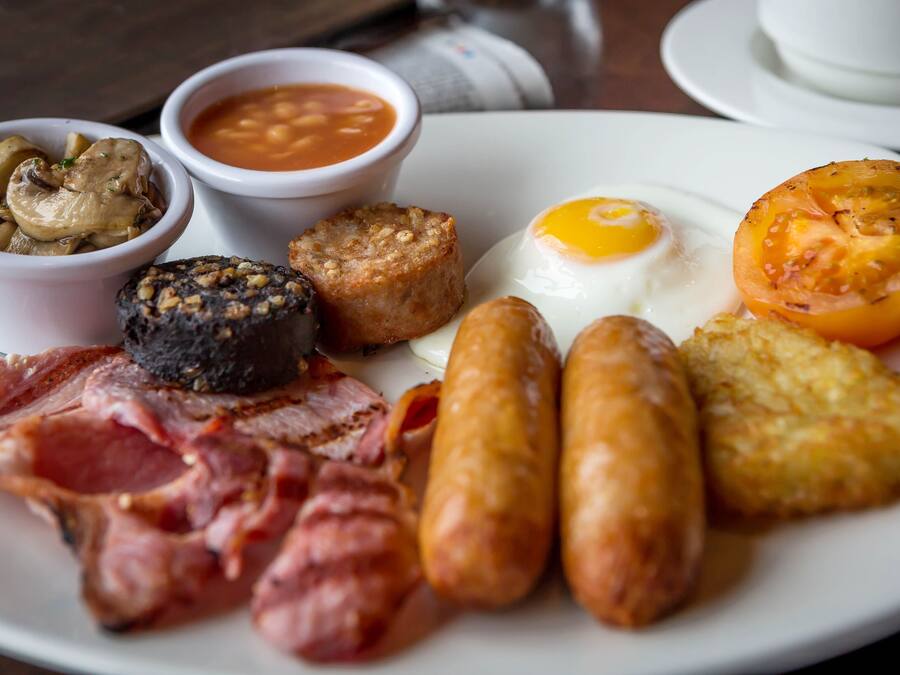 Prato de comida de café da manhã com salsichas, ovos, bacon, cogumelos, feijão e um tomate grelhado.